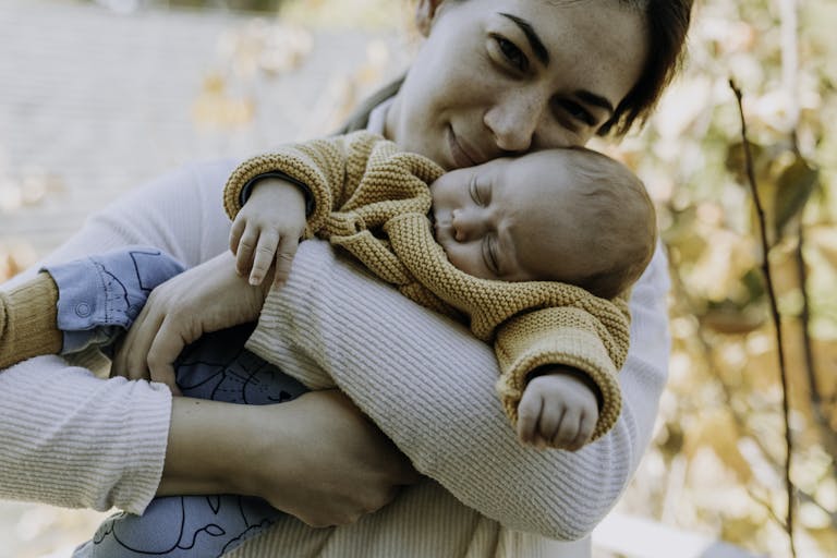 A tender moment of a mother hugging her sleeping baby in a cozy sweater outdoors.